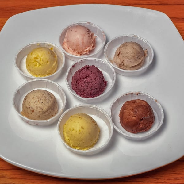 Seven small cups of colorful butter, including yellow, pink, purple, and brown, on a white plate.
