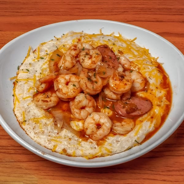Shrimp and grits with sausage, onions, and a rich red sauce, served in a white bowl.