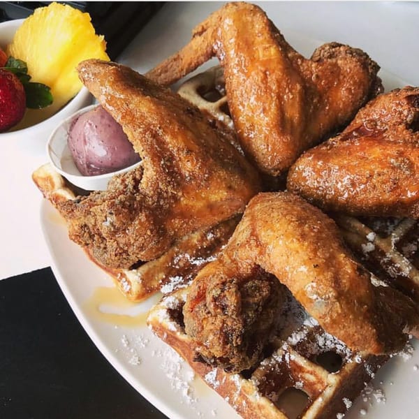 Dame's golden fried chicken wings and waffles, drizzled with syrup and powdered sugar, with fruit.