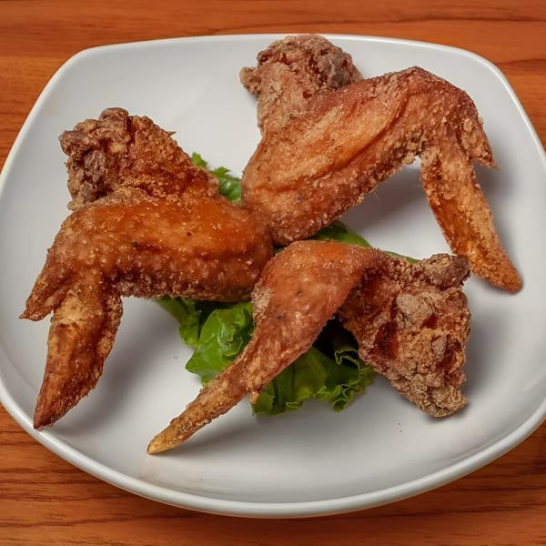 Three crispy fried chicken wings on a bed of green lettuce on a white plate.