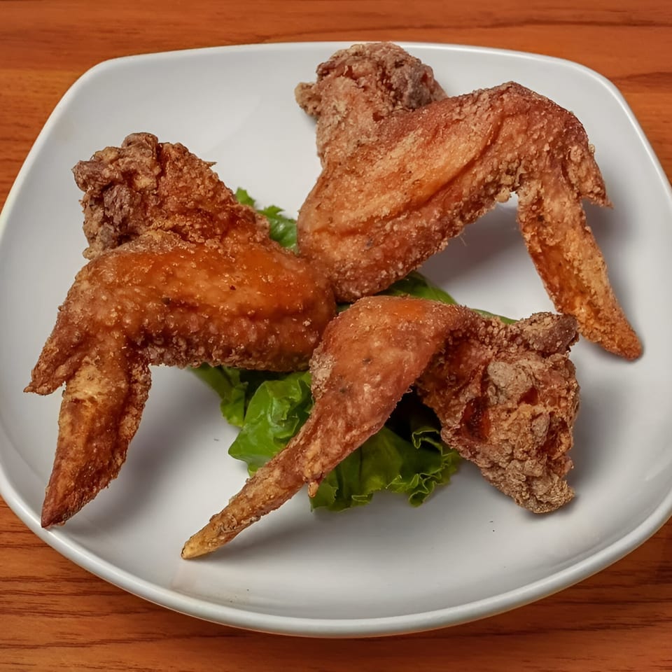 Three crispy fried chicken wings on a bed of green lettuce on a white plate.