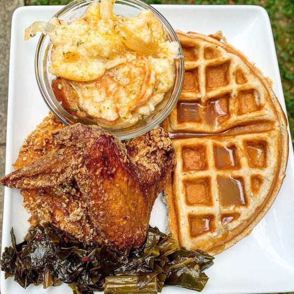 Dame's southern chicken and waffles with collard greens and shrimp and grits on a white plate.